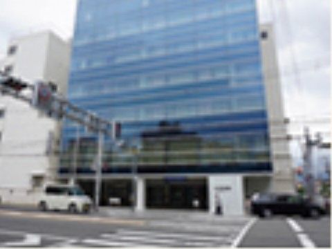 病院の前は横断歩道があり大きな道路が通っている。車が２台道路を走っている。建物には窓がたくさんある。