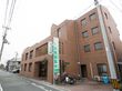 ブラウン調のマンション風の施設外観になっている。施設名が記された看板が設置されている。駐輪場にバイクと自転車が停まっている。