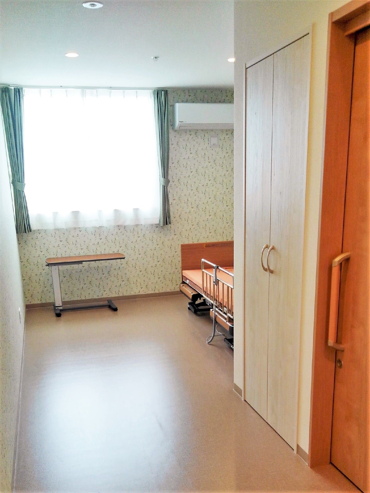 縦長の間取りの居室、手前側には引き戸があり、奥にはベッドが置かれている。