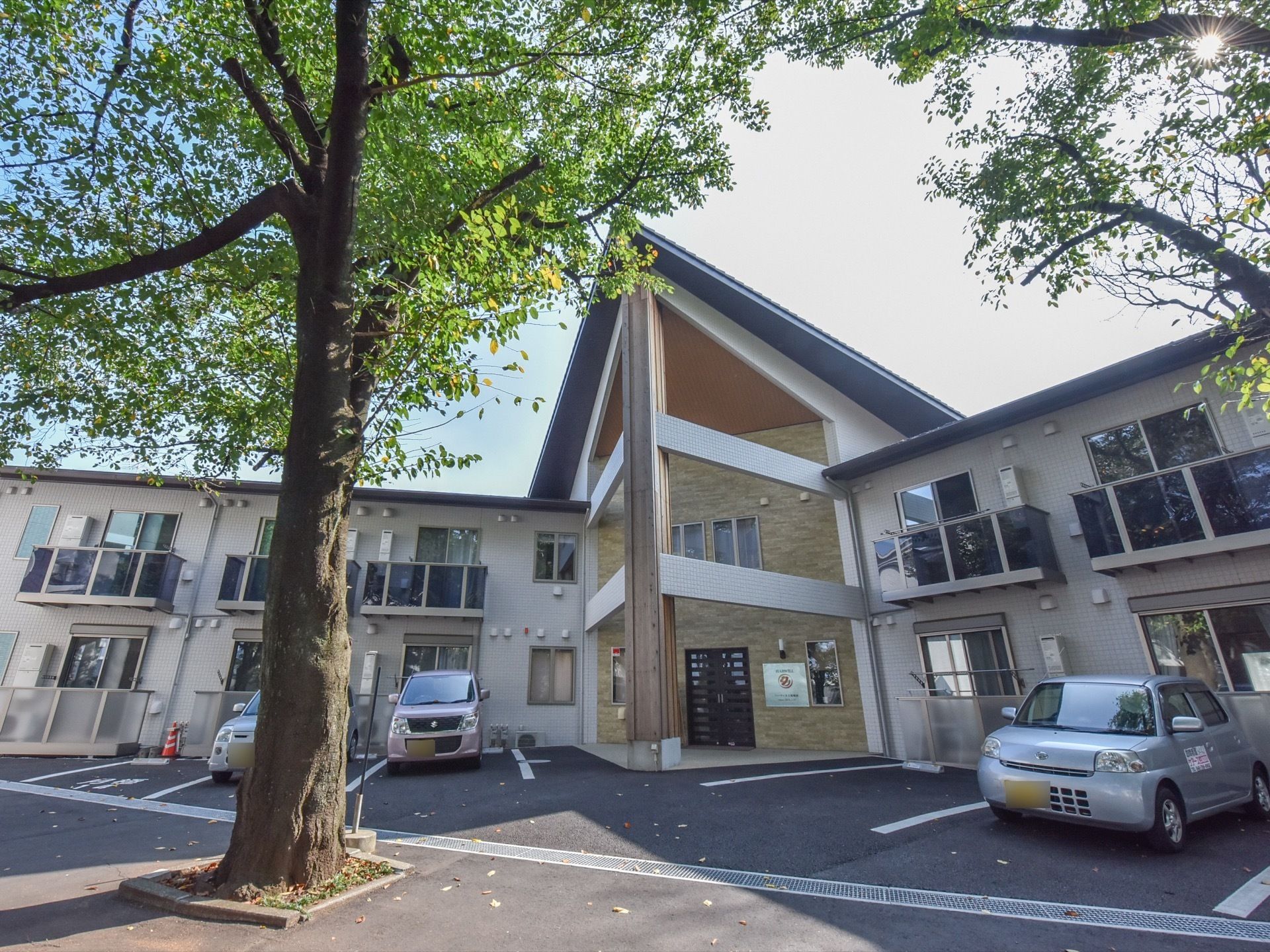 施設の敷地内に駐車場が完備されている。入口をはさんで両サイドに数台ずつ停められる。手前には大きな木が植えられている。