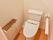 温水洗浄便座、左側に可動式の手すりが設置されている。トイレットペーパーは２つ並べてセットできるタイプである。