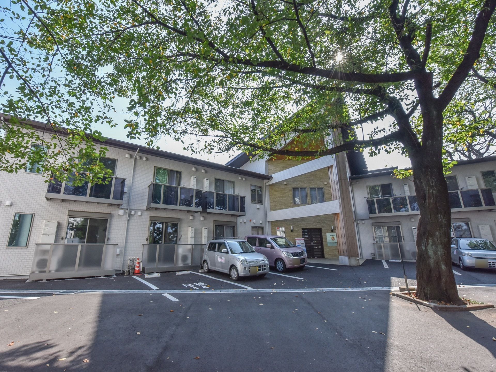 玄関を真ん中にして、両側に居室がある作りの建物になっている。敷地内に駐車場があり、手前には大きな木が植えてある。