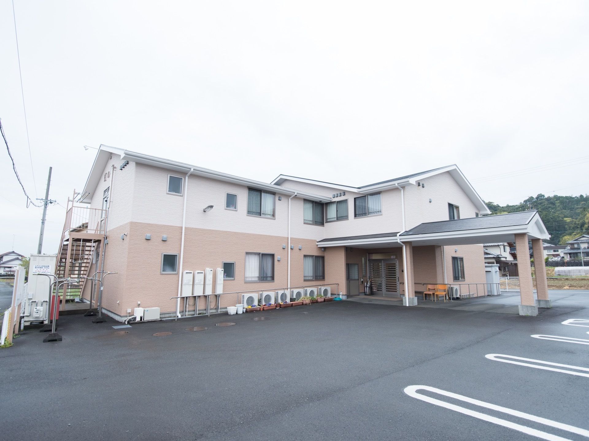 施設は白とベージュの２色使いである。敷地内に駐車スペースがあり、複数台の車を停めておくことができる。