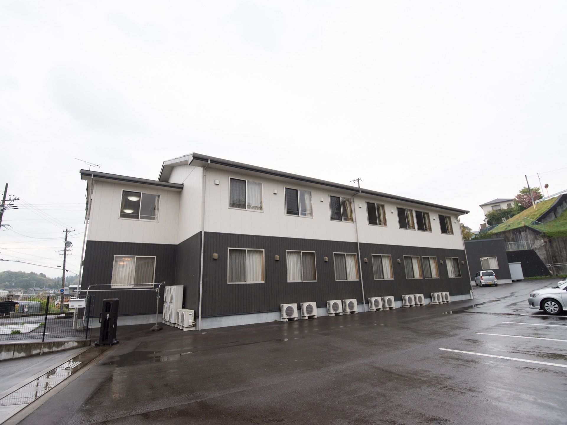 施設は２色の外壁になっている２階建ての建物である。広い駐車場があり、ご家族が来訪する際も安心して停めることができる。