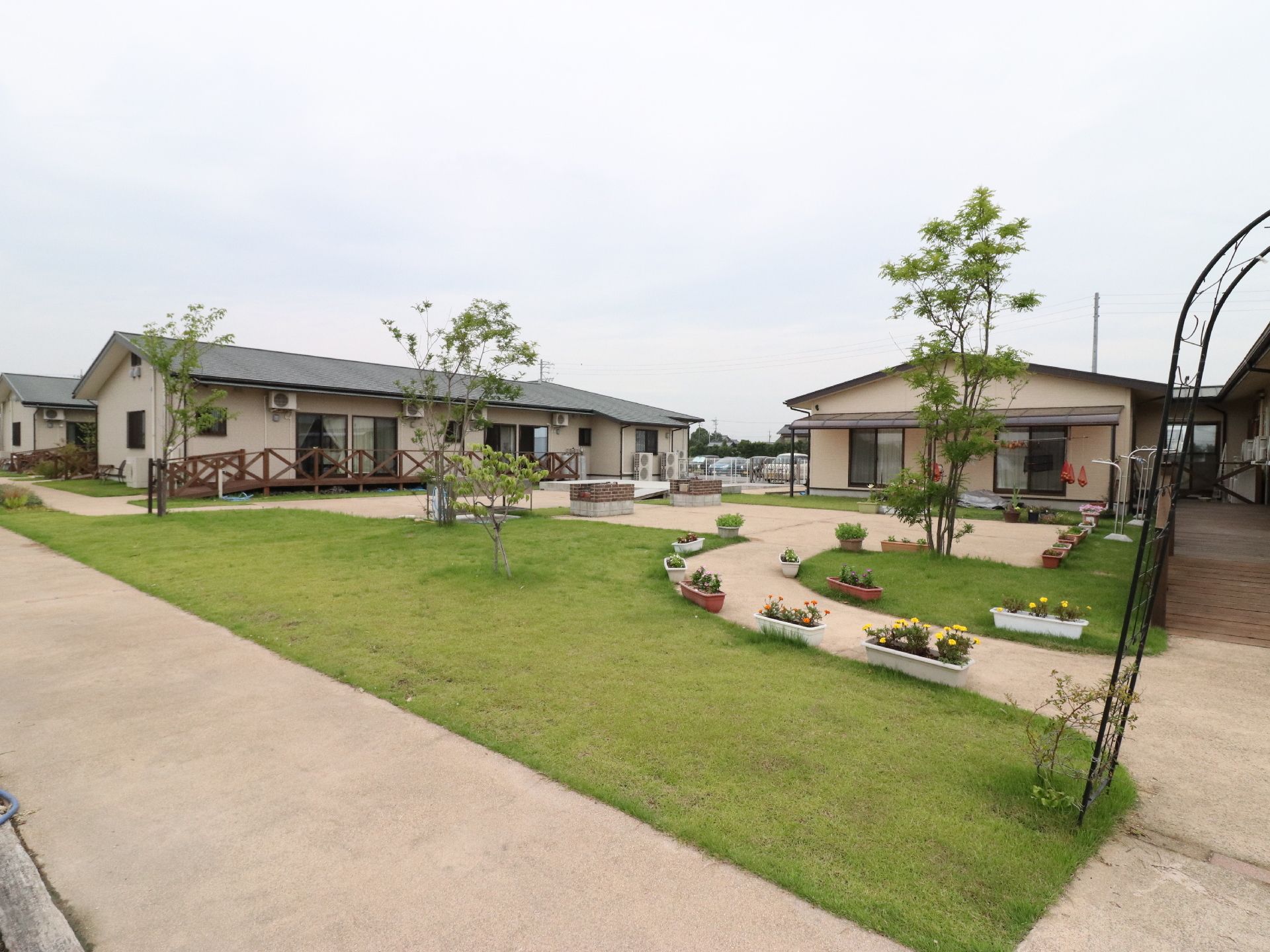 整えられた芝生と花が植えられたプランターが並んでいるアプローチ、平屋の建物が並んでいる風景