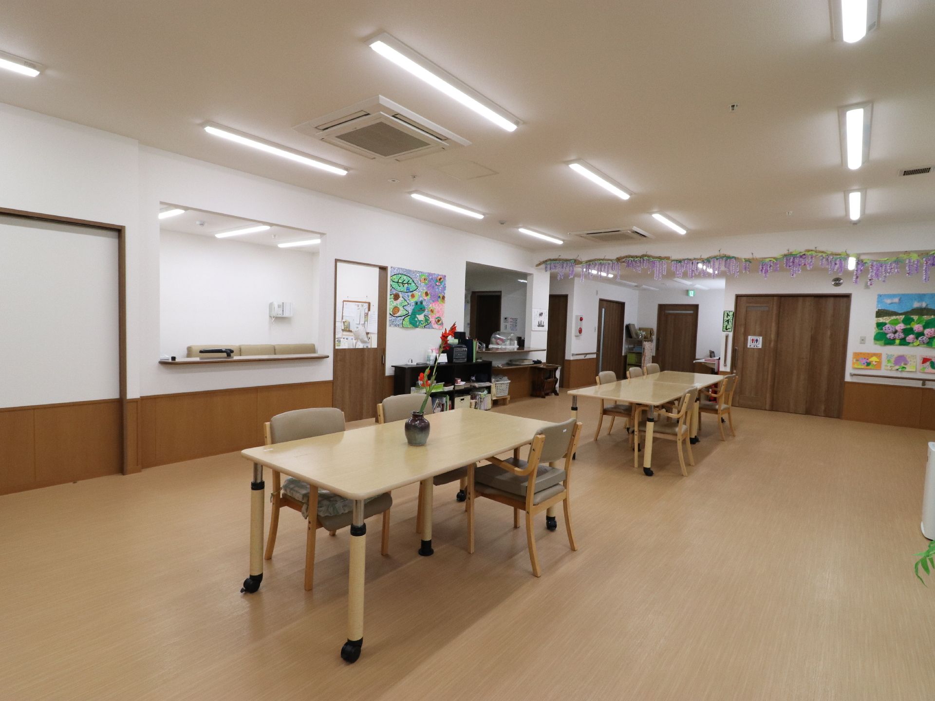 テーブルの上には花が過敏に飾られている。奥には棚があり本が設置されている。壁にはカエルの絵がかけられている。