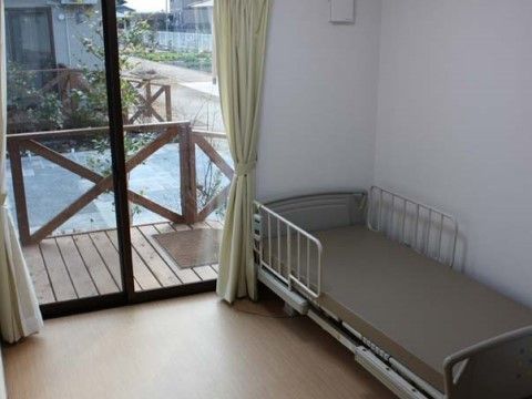 掃き出し窓の外にウッドデッキのある、ベッドが置かれた居住スペース