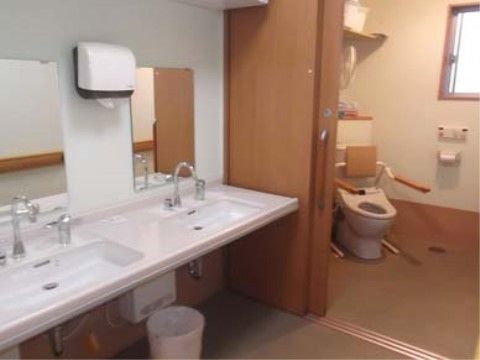 トイレの入り口のスライドドアが開いていて、斜めに設置された洋式便器が見える。便器に背もたれと手すりが取り付けられている。