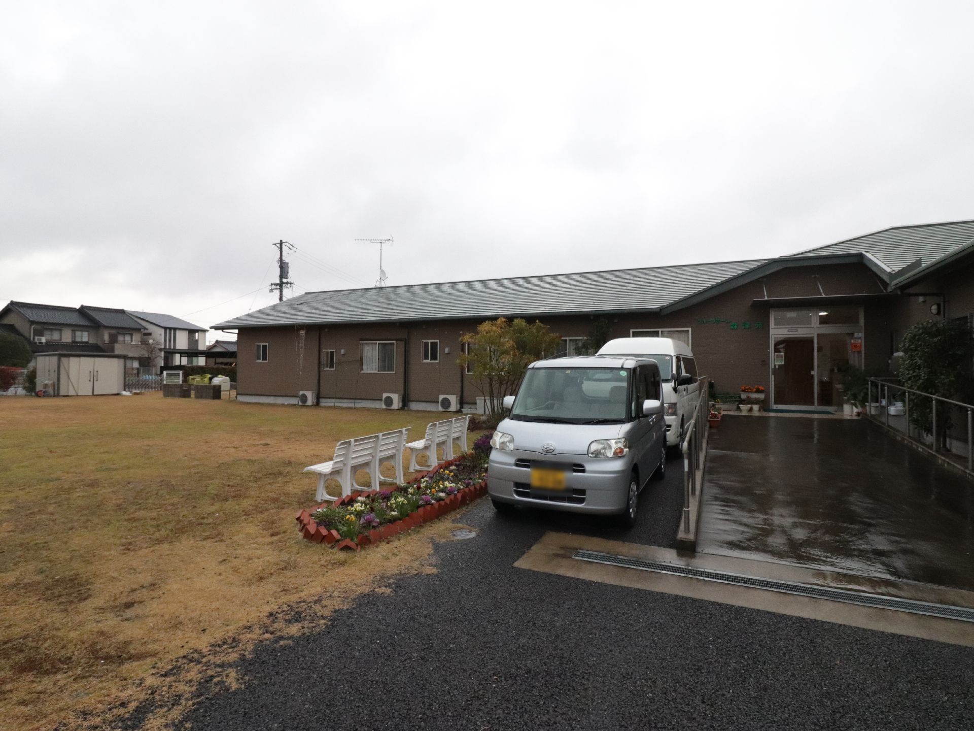 施設の外には丁寧に手入れが行われた芝生が広がっている。その端にはベンチが２台設置してあり、花壇もある。
