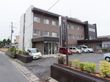 ３階建ての施設である。看板や建物の壁の一部に濃い茶色が使用されており、上品で重厚な雰囲気である。植栽があり、緑も感じられる。