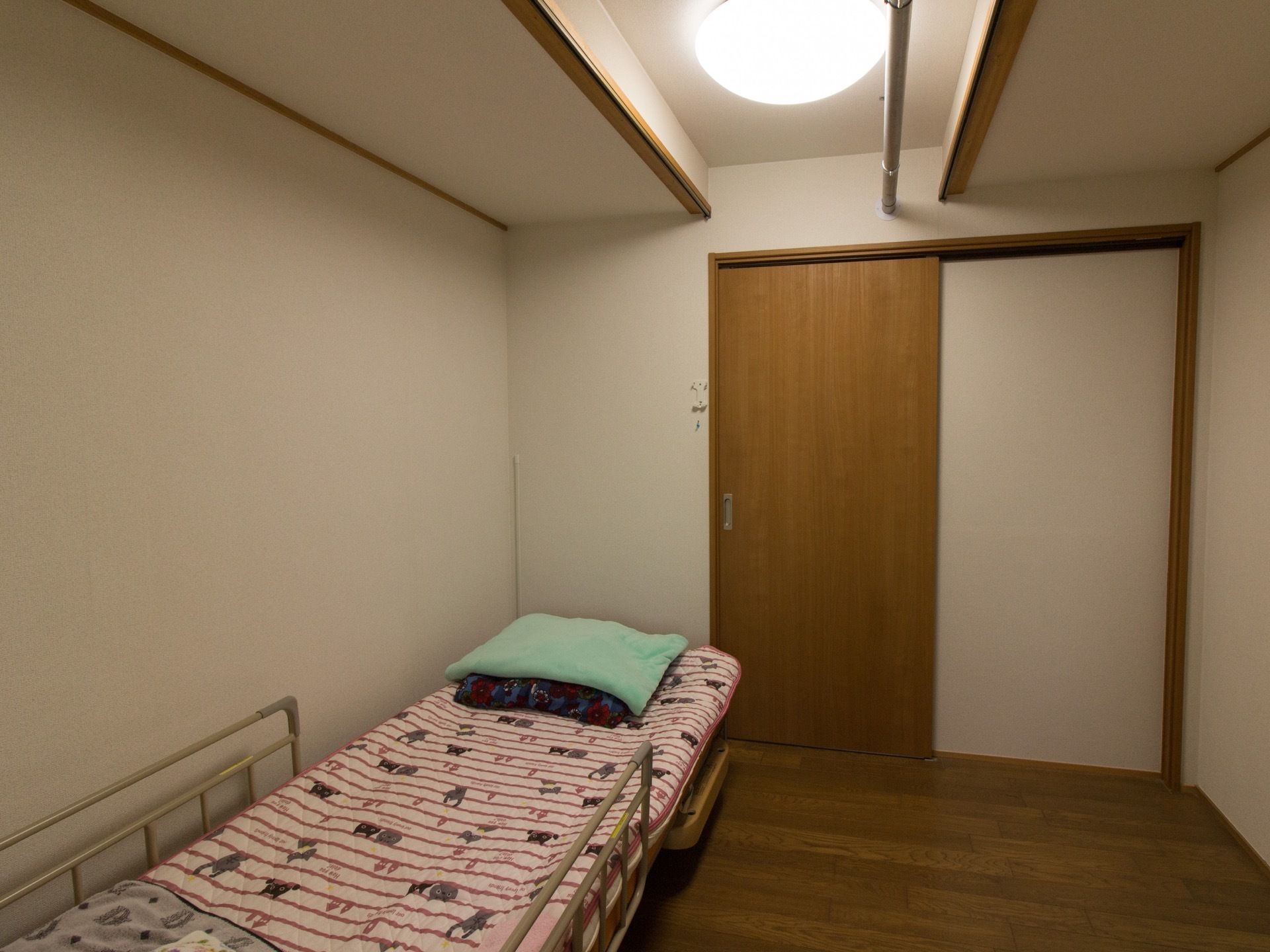 フローリングの部屋に電動の介護用ベッドが設置され、毛布が置かれている。部屋のドア木製でスライド式になっている。