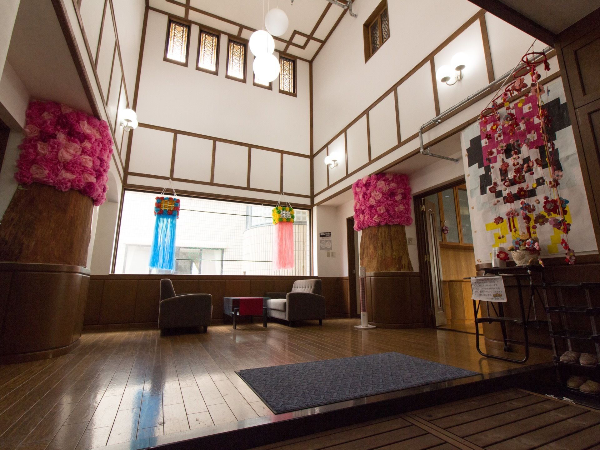 レトロな雰囲気の玄関になっている。紙で作られた桜の造花や、天井飾りがついている。奥にはソファとテーブルが置かれている。