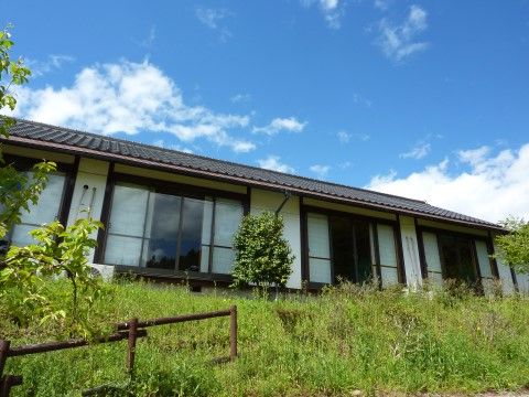 緑豊かな環境にある、大きな掃き出し窓がいくつも並んでいる平屋の建物