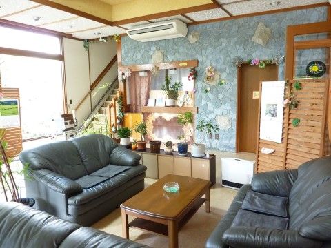 ３台の大型ソファーとテーブルが置かれている。台の上にはいくつもの植木鉢が飾られ、奥にトイレや階段が見える。