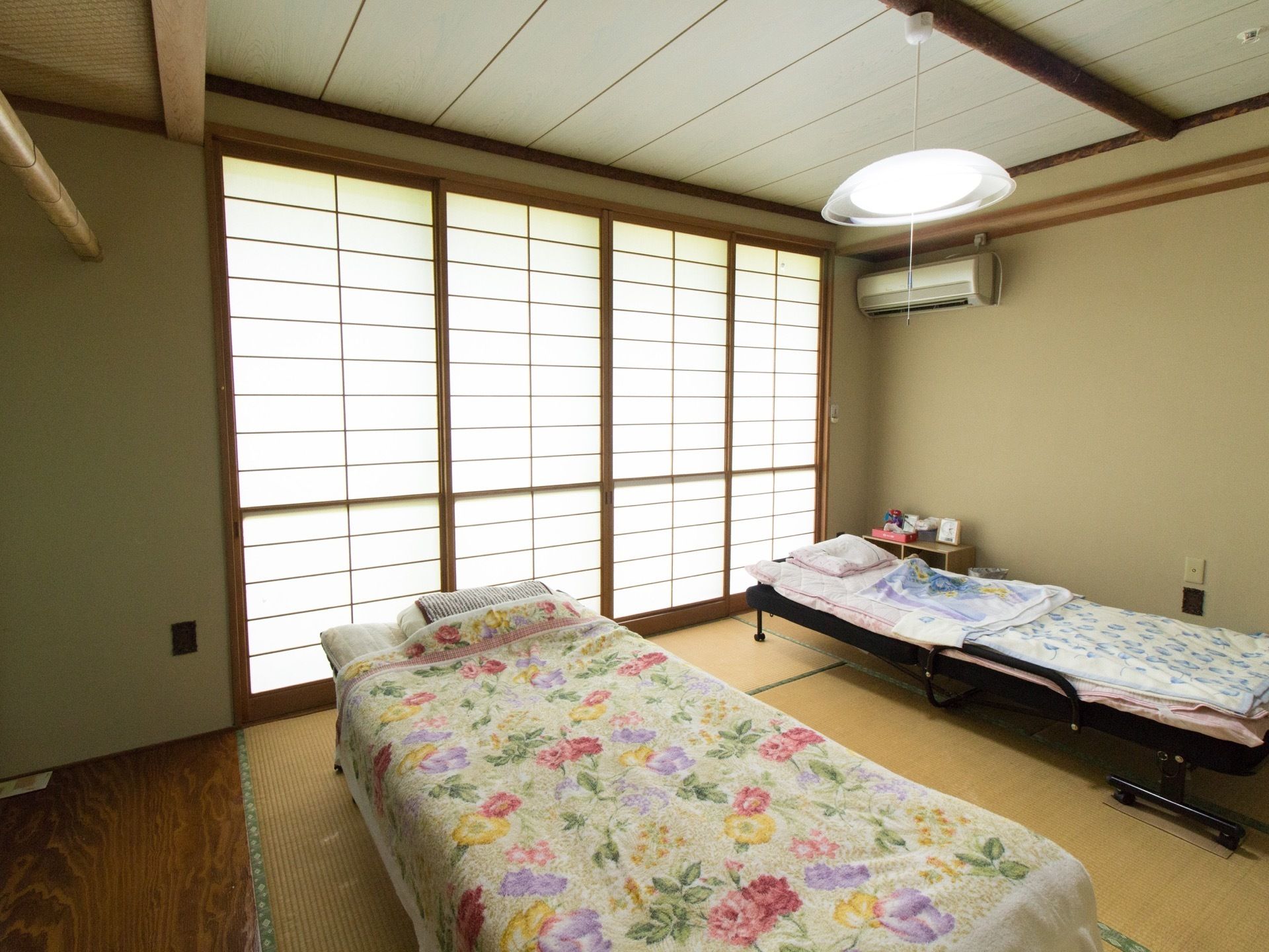 居室は和室タイプで、畳敷きになっている。窓には障子が閉められている。組み立て式のベッドが２台置かれている。