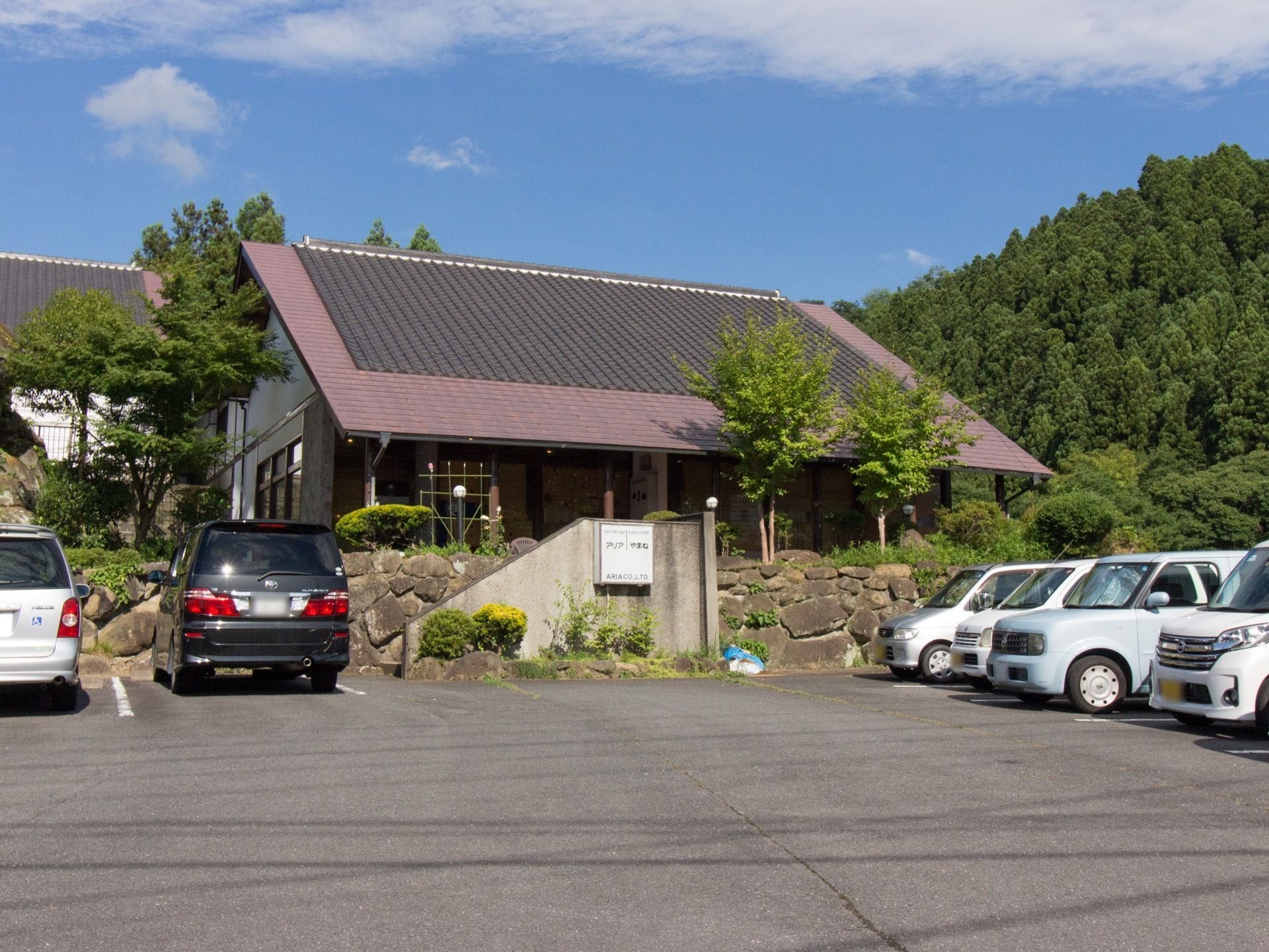 大きな三角の屋根が乗った建物で、石垣の上に建っている。施設前には駐車場が完備されていて、植栽に囲まれている。