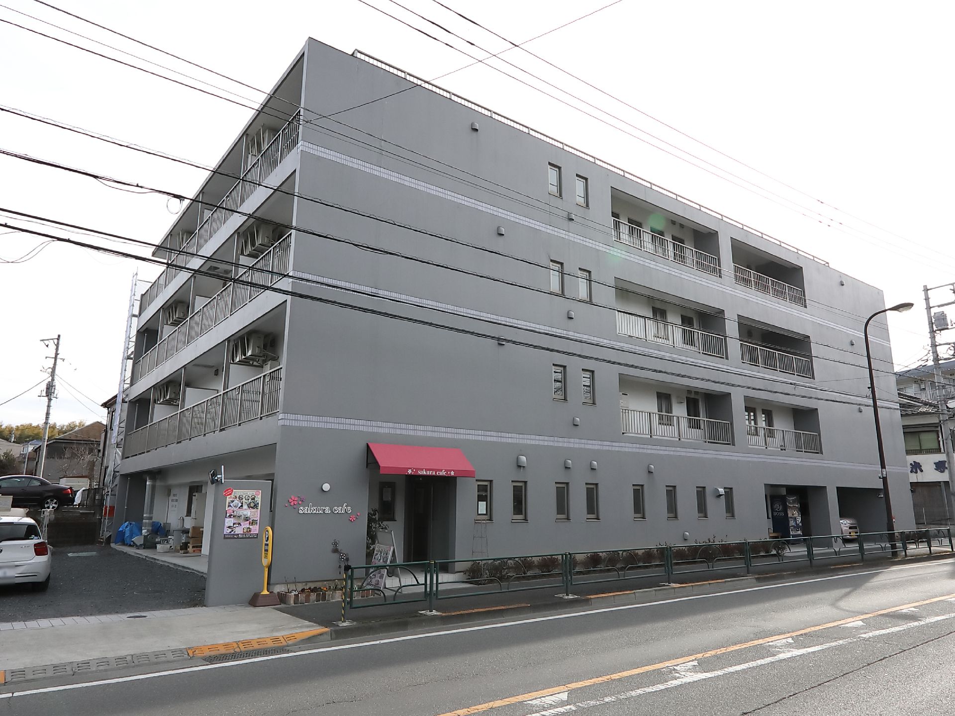グレーの外壁の４階建ての建物である。１階に併設しているカフェの入り口があり、赤いテントが取りつけられている。