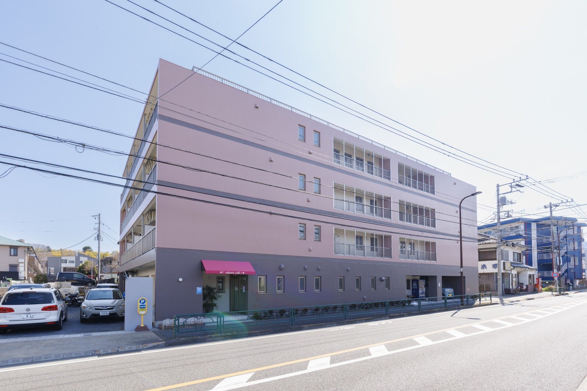 グレーの外壁の４階建ての建物である。１階に併設しているカフェの入り口があり、赤いテントが取りつけられている。