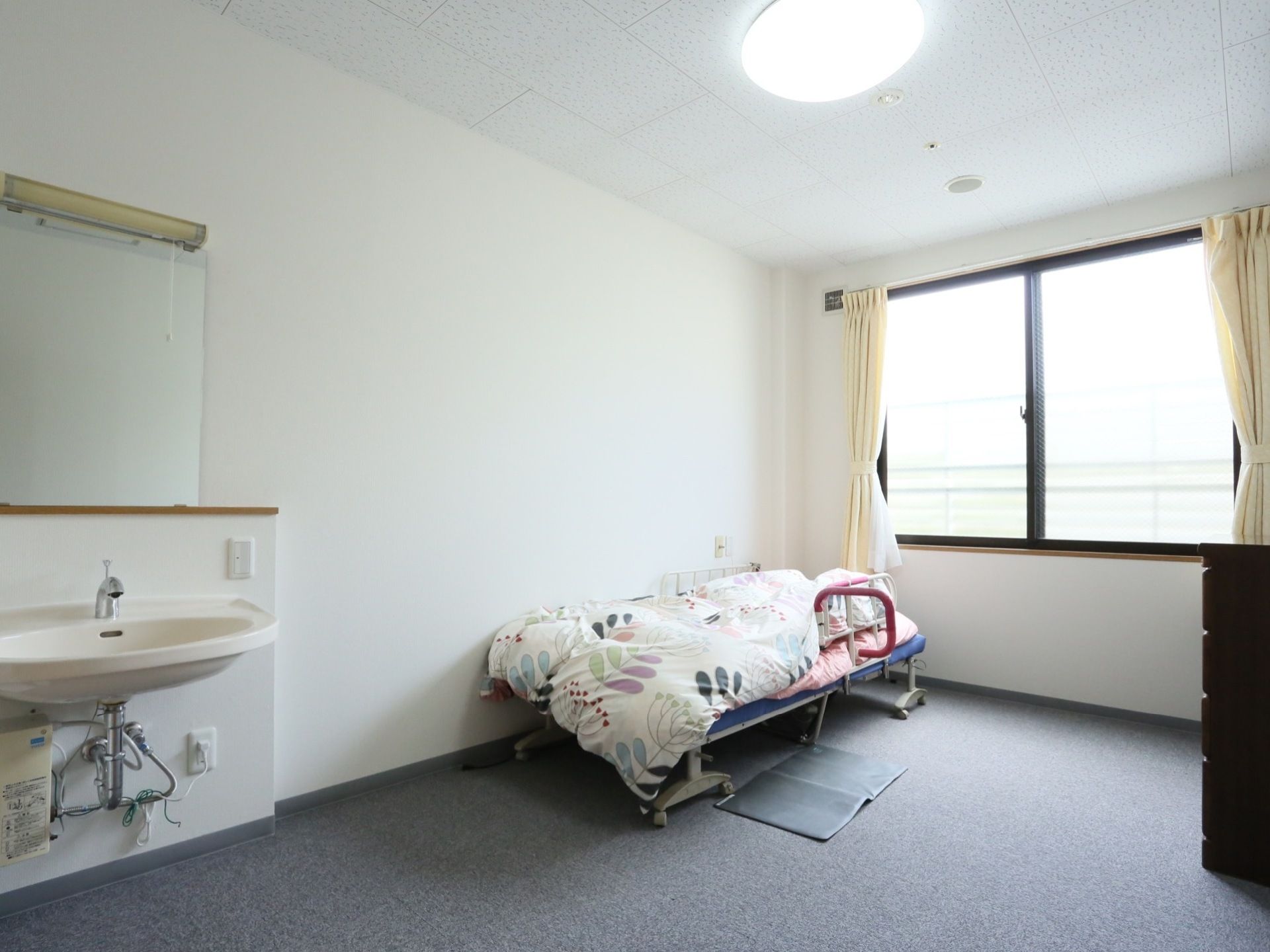 広い居室で、ベッドと家具を置いても十分な広さがある。洗面台が備え付けられており、近くには照明のスイッチがある。