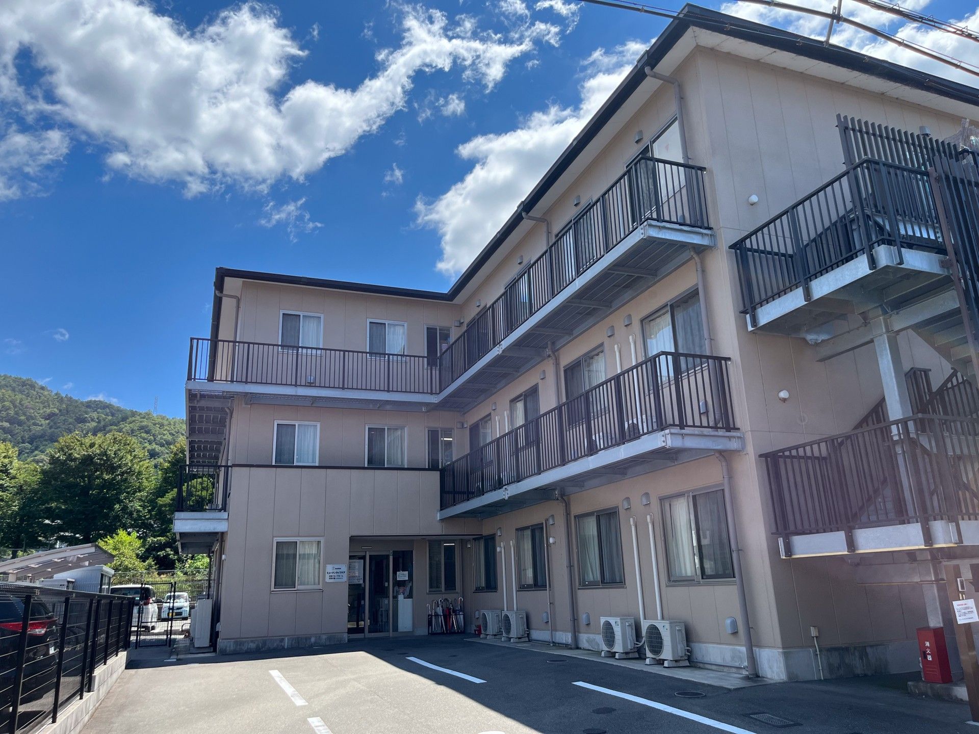 クリーム色の外壁で、ベランダが並んだ三階建ての施設建物