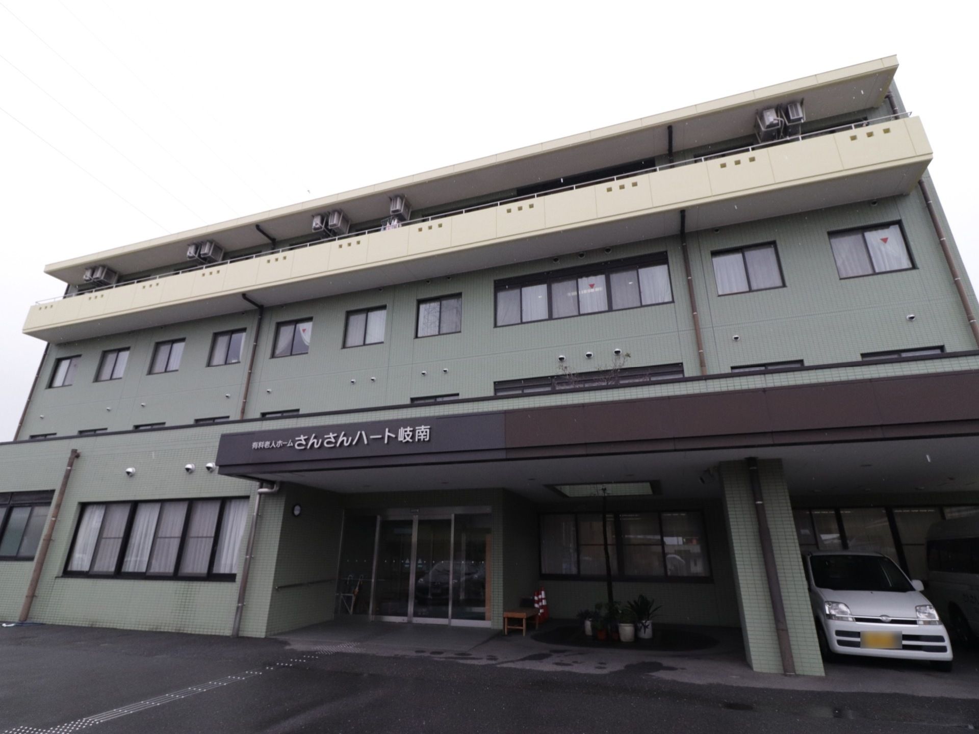 大きな文字で施設名が書かれた長方形の屋根が、出入口の上部に設置されている。白い植木鉢に入った草花が置いてある。