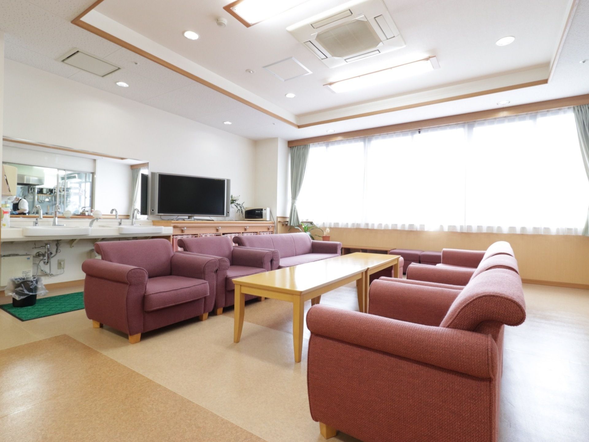 ベージュ色のテーブルの左右に、色違いの豪華なソファーが設置されている。壁際にはテレビがあり、その横には洗面台がある。