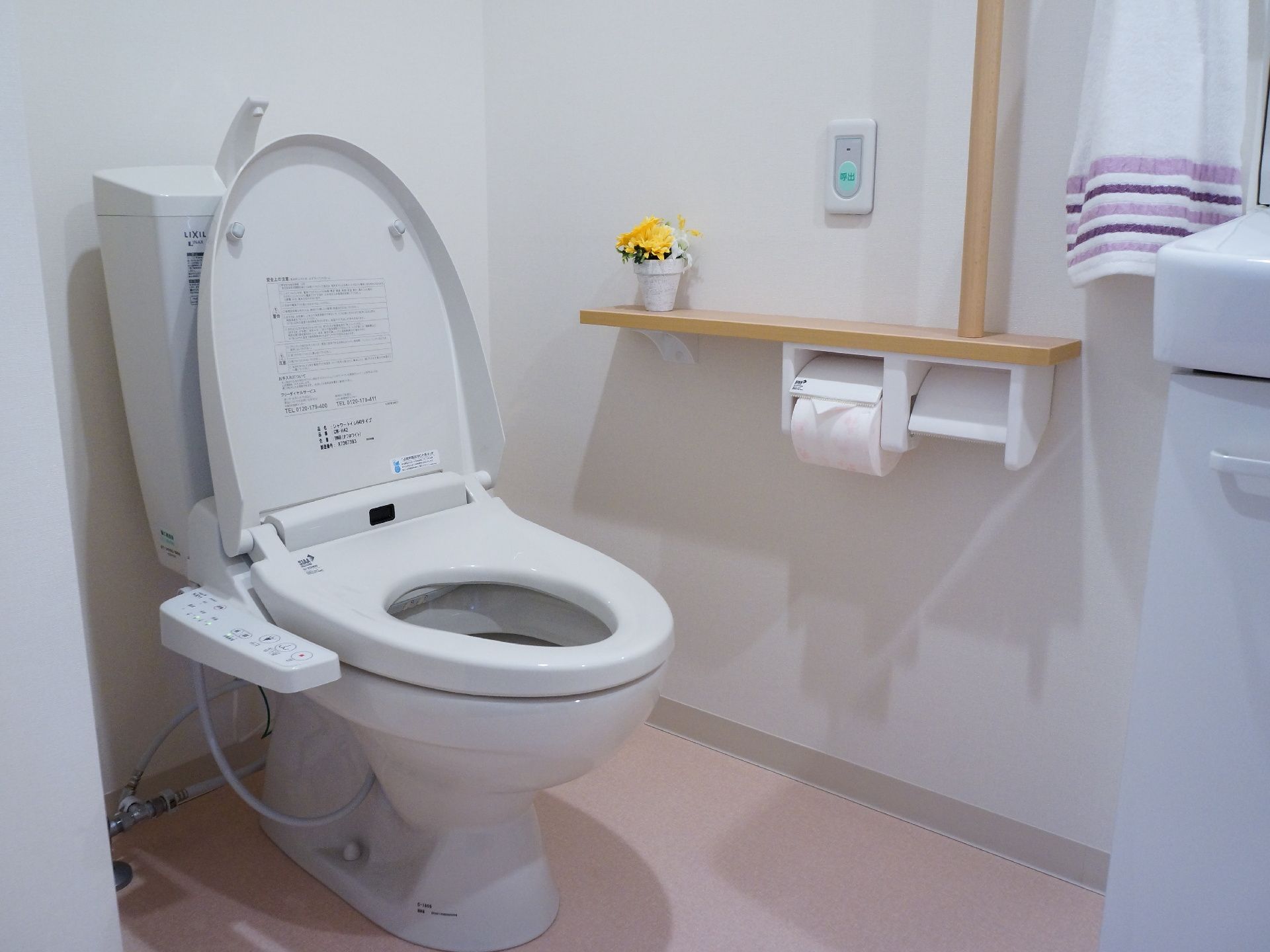 温水洗浄便座付きトイレがあります。左手に手すり付きペーパーホルダーがあります。ホルダーの少し上に緊急時のボタンがあります。