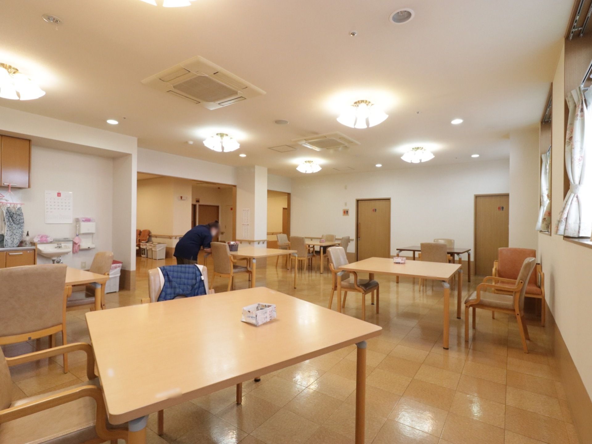 リビングの様子。木製の正方形テーブルがあり、それぞれ椅子が数脚置かれている。床は、木目調のフローリングである。