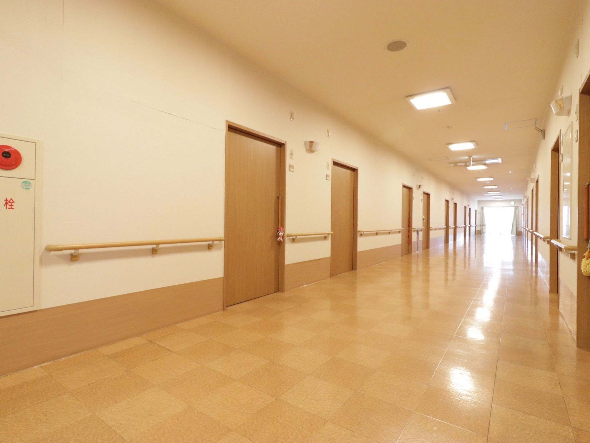 廊下がまっすぐ伸びている。正方形の板が組まれたフローリングの床で、廊下の両側に居室のドアが並んでいる。