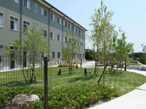 グレーの外壁の建物である。目の前には青々とした芝生が広がっており、ところどころに照明が設置されている。