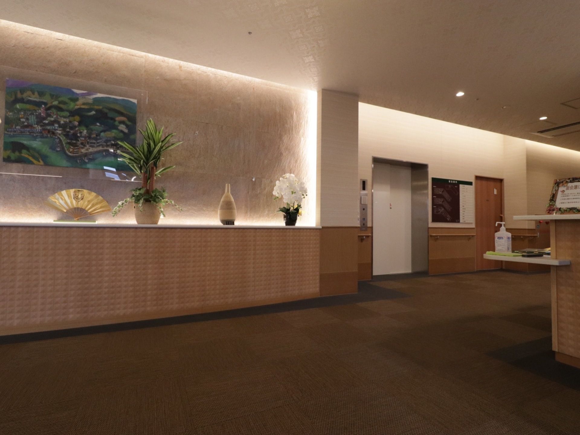 ロビーには扇や壺、花や絵画などが飾られている。全体的に落ち着いた照明で、奥にはエレベーターが設置されている。