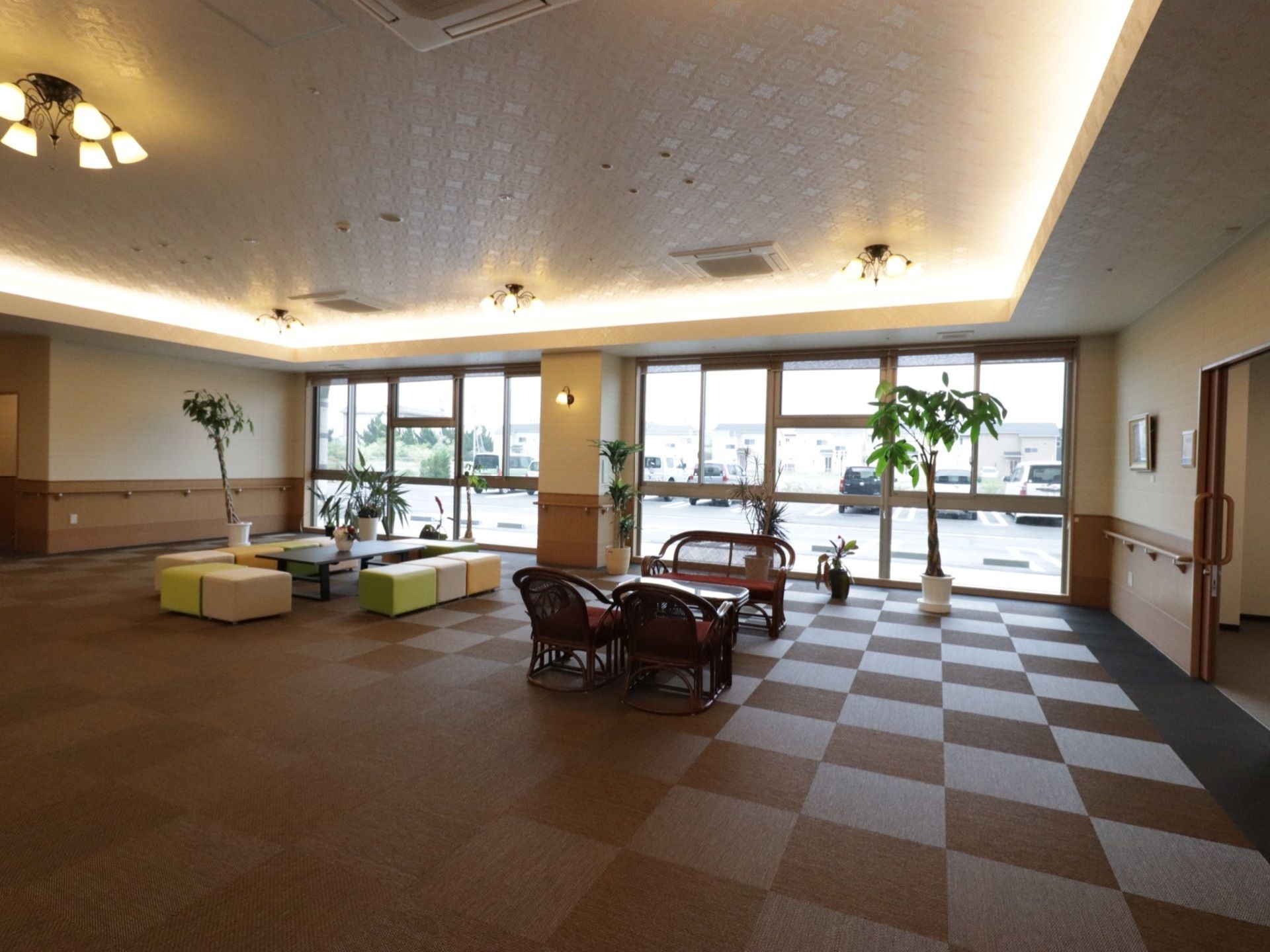 広いロビーには椅子とテーブル、観葉植物が置いてある。壁には手すりが設置してあり、片側の壁一面は窓ガラスとなっている。