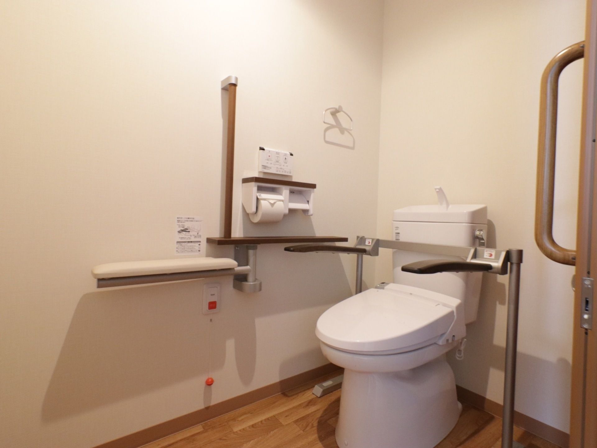 スライド式の扉のトイレルーム内は、温水洗浄便座の両側に手すりが設けてあり、壁にも手すりとタオルハンガーが備えてある。