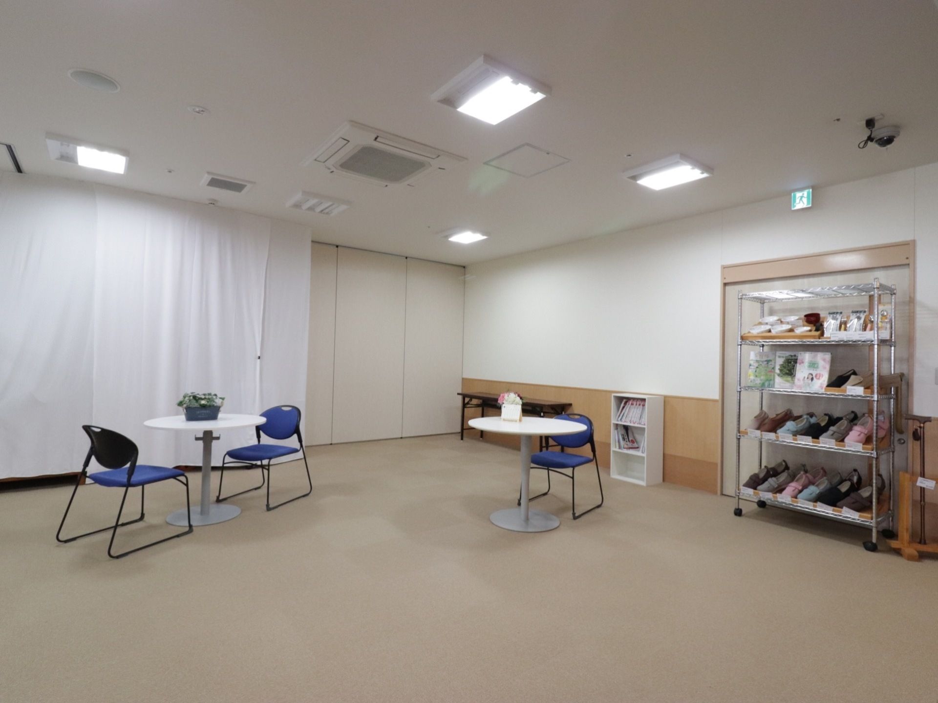 明るい雰囲気の共有スペース。白い丸テーブルとブルーの椅子が置かれている。食器や靴の見本が飾られている。