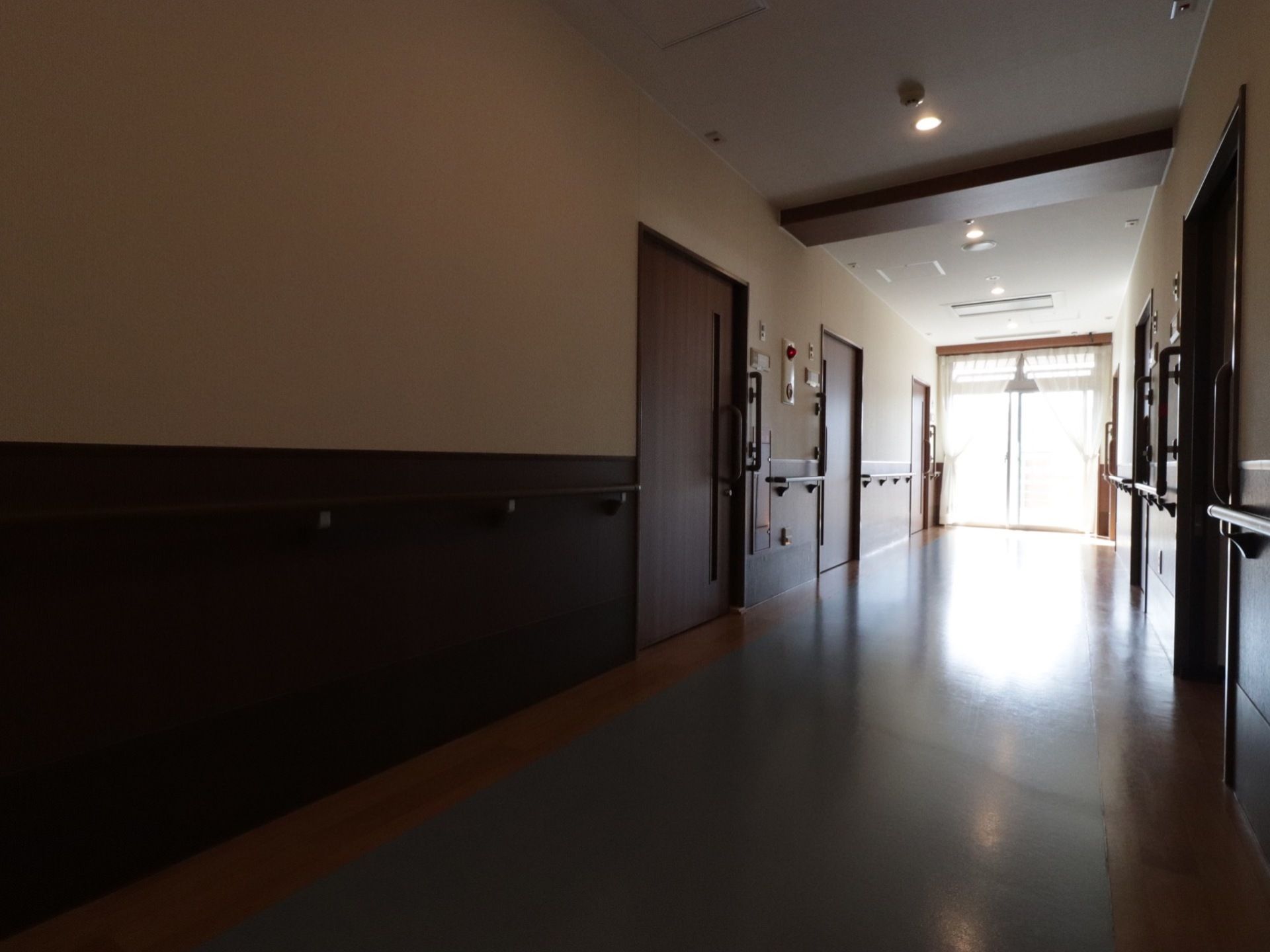 ダークブラウンを基調とした落ち着いた雰囲気の廊下。幅が広く、壁の両サイドには手すりが設置されている。