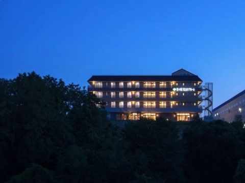 木々に囲まれた中に建つ、夜間でも明るくライトアップされた施設建物