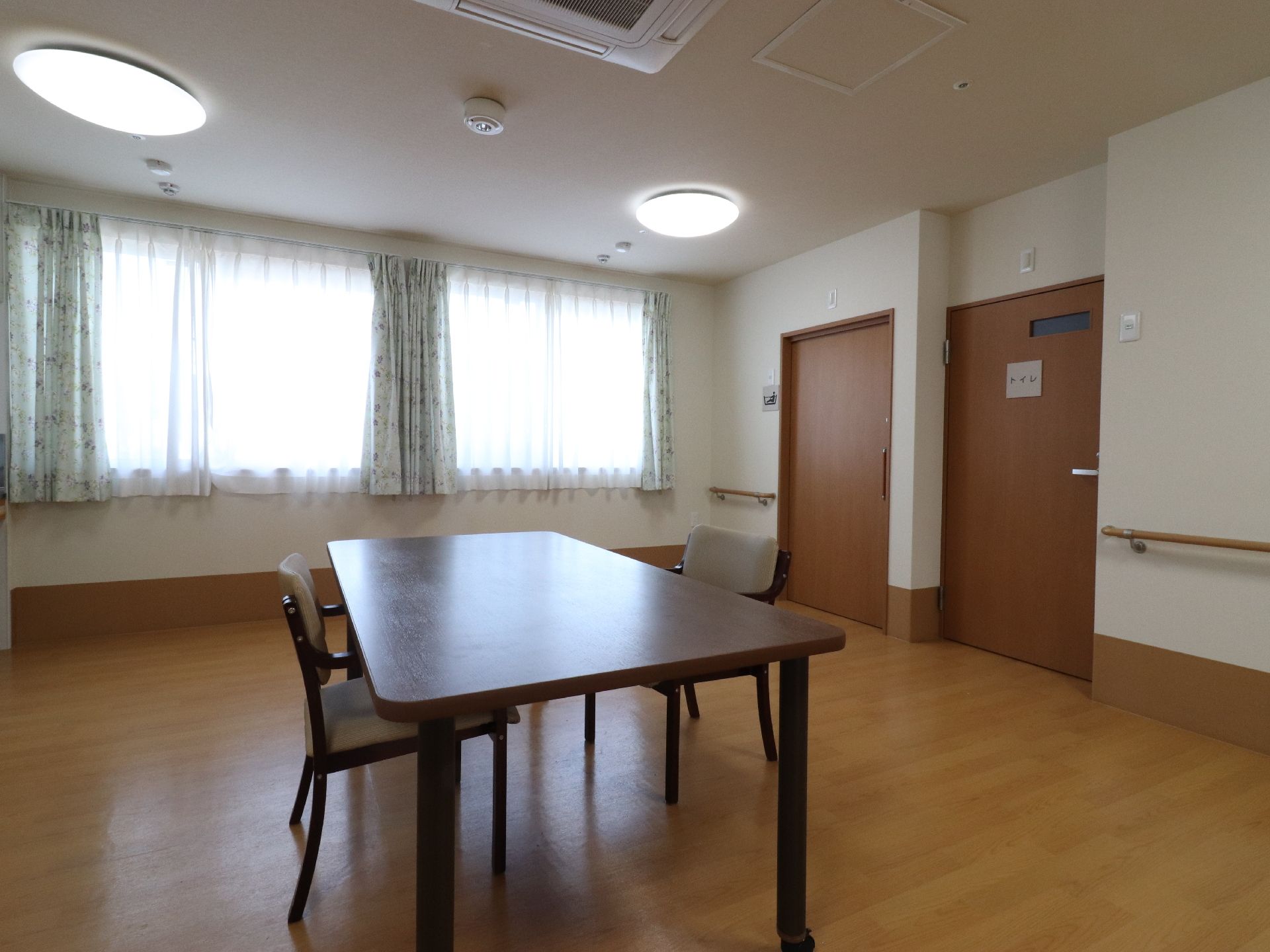 多目的ルームの中央には、キャスター付きのテーブルがある。また、椅子が2脚置かれている。トイレと浴室のドアが見える。