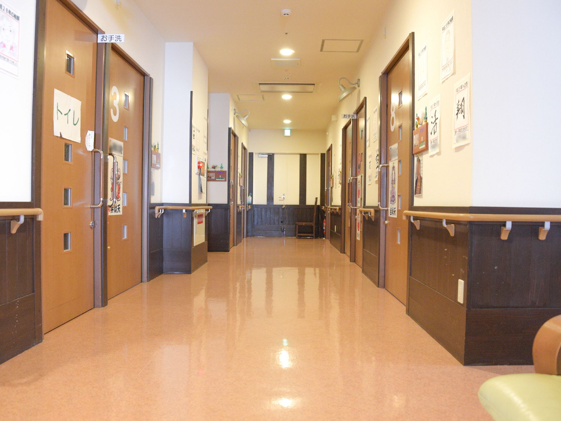 居室前の廊下はバリアフリー、手すりが設置してあるほか、共有トイレが設置してある。廊下の角に木製の椅子が置いてある。