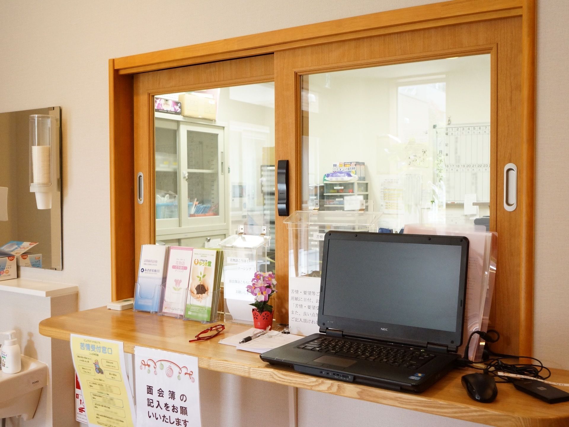 施設玄関に設置されている受付である。カウンター上には面会者名簿やパンフレッド、パソコンが設置されている。