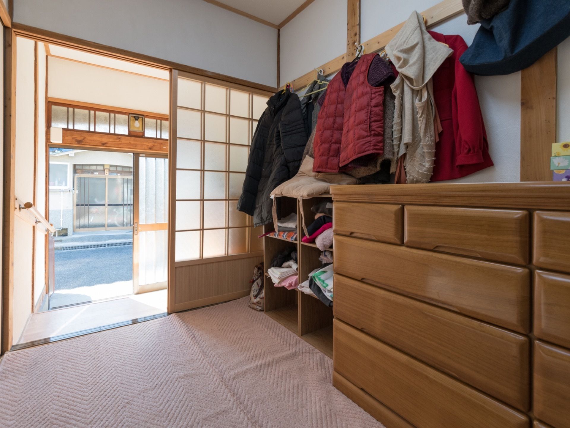 畳の上にはマットが敷かれており、その上にタンスが置かれている。壁には上着などの衣類がかけられている。