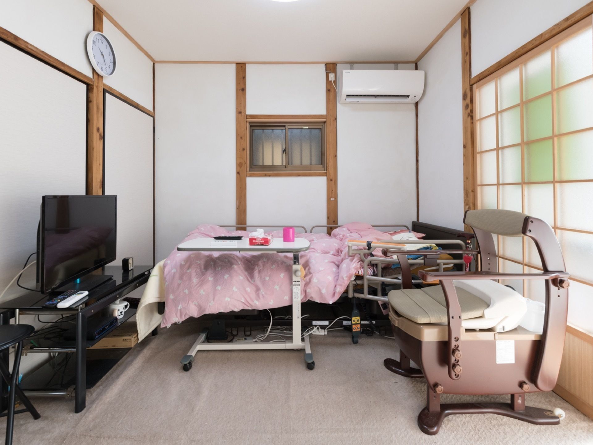 介護ベッドとテレビ、ポータブルトイレが設置されている居室である。和テイストで、障子から日が差し込み明るい雰囲気。