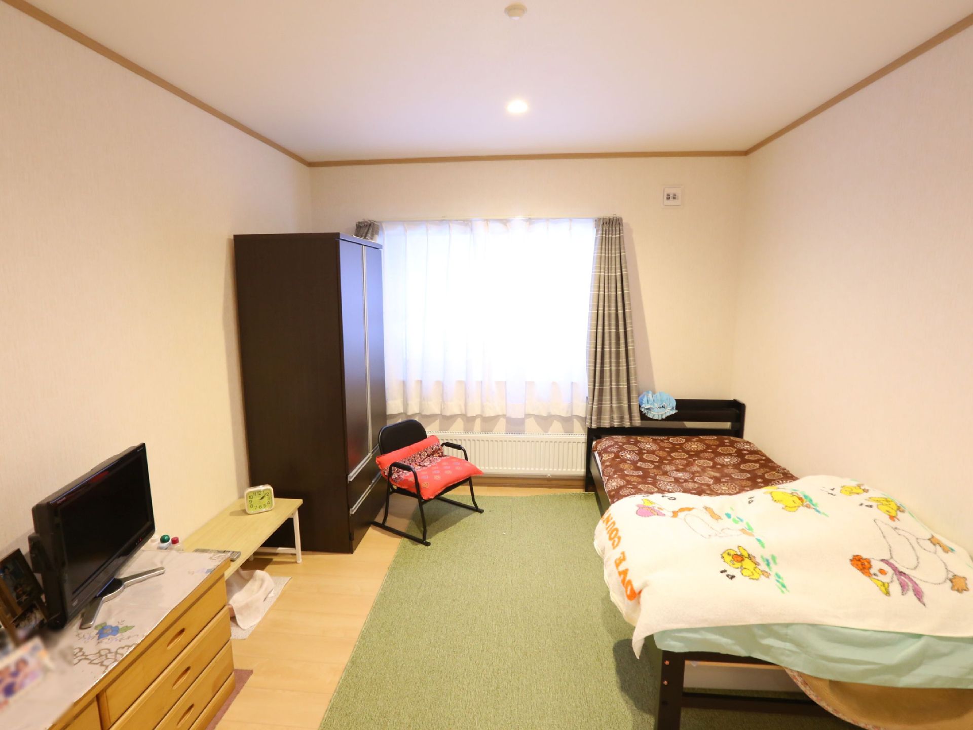 収納やテレビ、テーブルなどが壁際に置かれた、一人部屋の居室