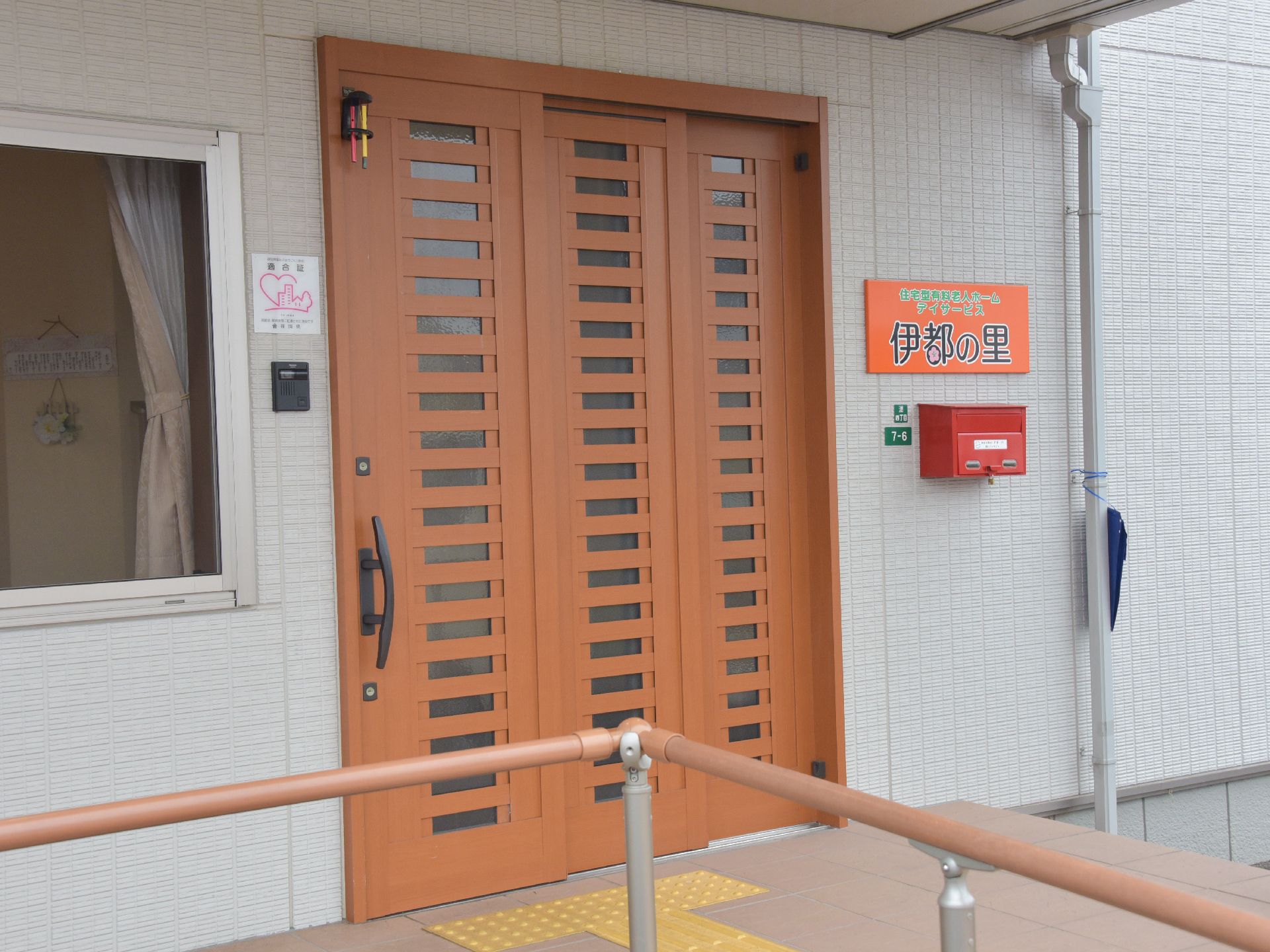入口に手すりのついたスロープのある、瓦屋根で白い壁の二階建ての施設建物