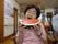 共有スペースで椅子に腰かける女性の入居者様が、両手でスイカを持ち、大きな口で食べようとする姿で、カメラのレンズに向かいポーズをとっている。