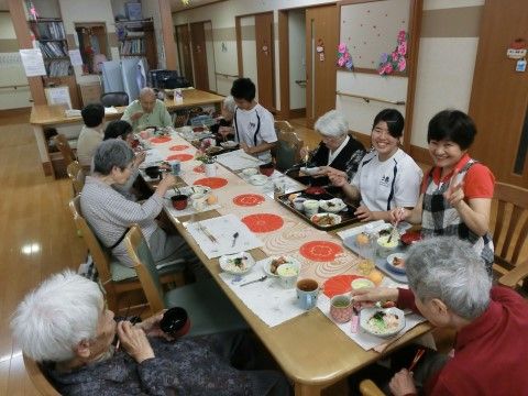 長テーブルで談話しながら食事をとる入居者様とスタッフ