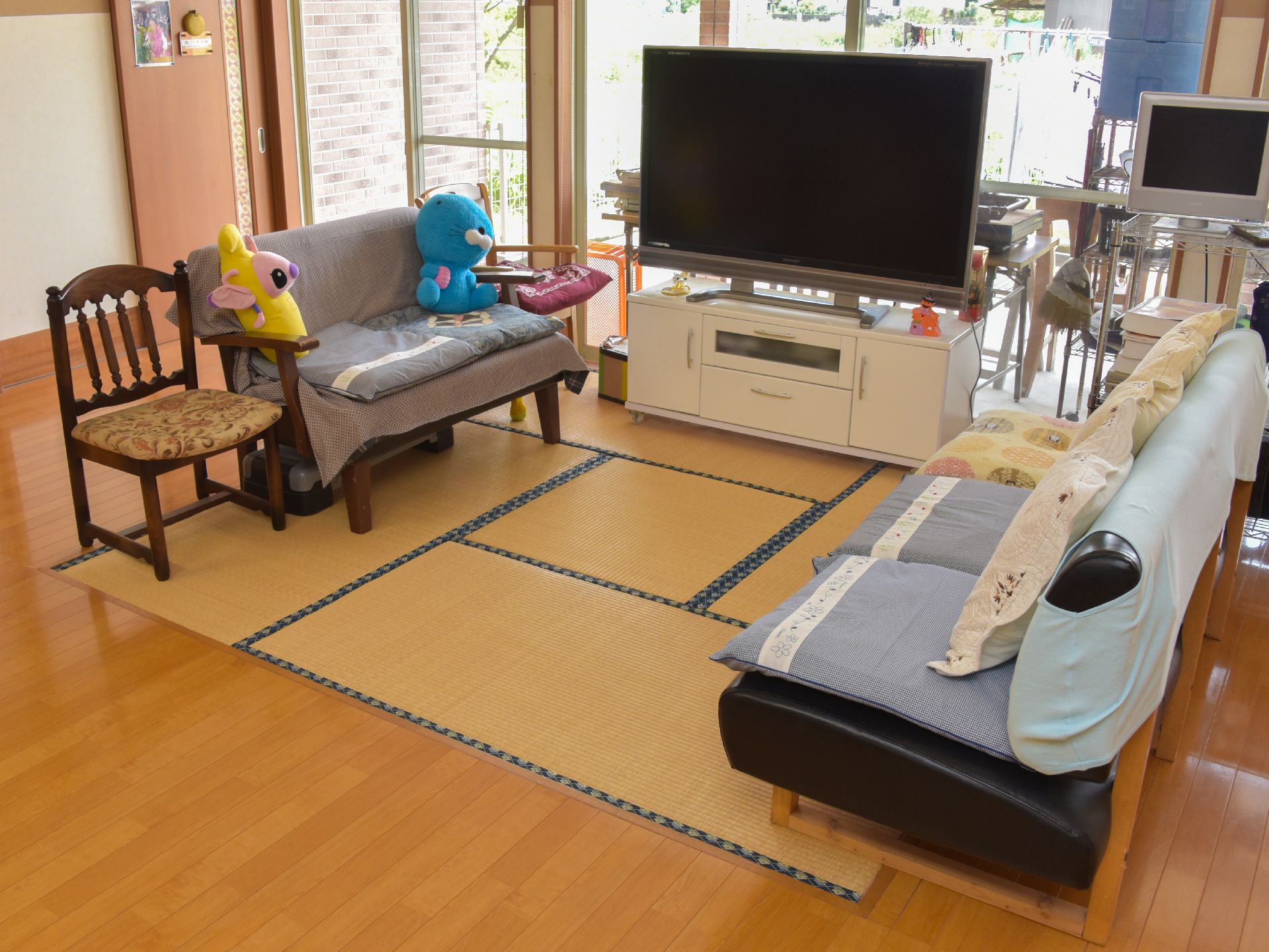 フローリングのダイニングに続いて和室のリビングがある。畳の上にTV台があり、椅子やソファが置いてある。