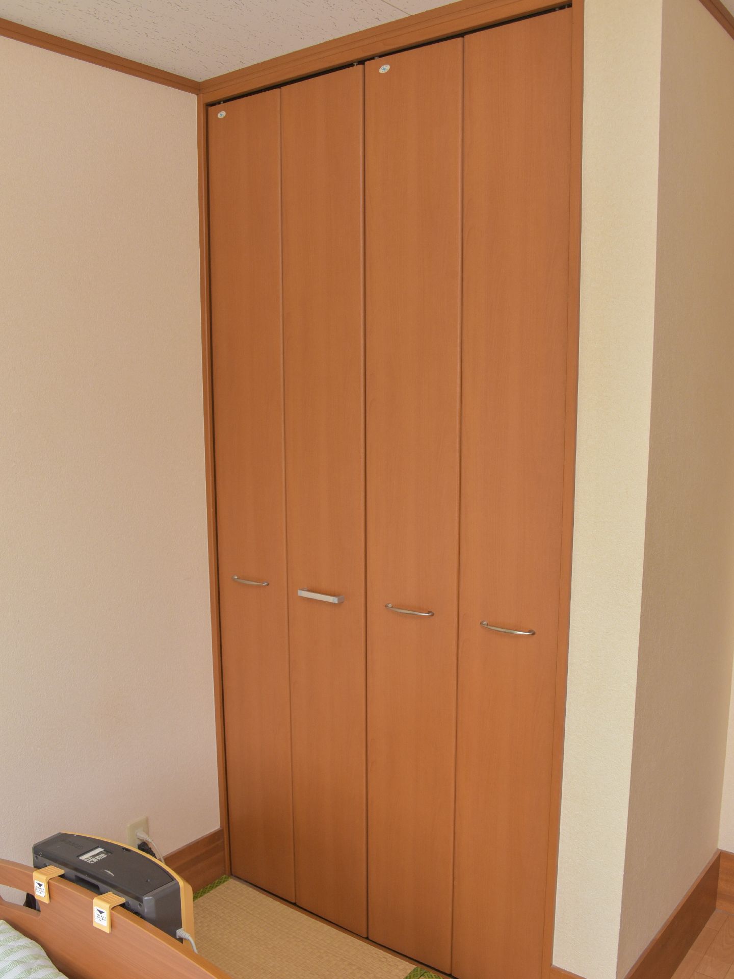 和式の部屋である。電動のベッドが置いてある。観音開きの一間サイズの収納が取り付けてある。床がフローリングの部分もある。