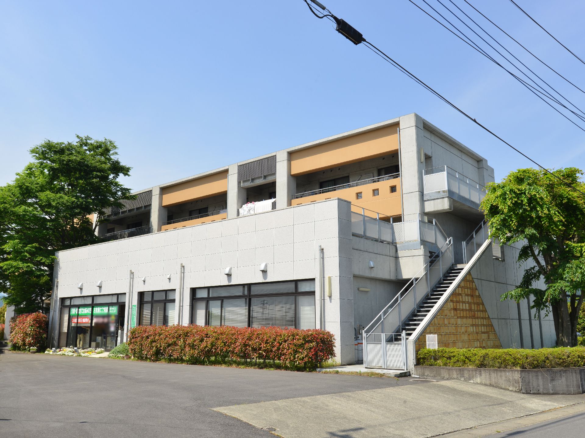 施設の左右に大きな木と、低木が植えてあり、垣根になっている。花壇がある。外階段がついており、2階3階部分へ行くことができる。
