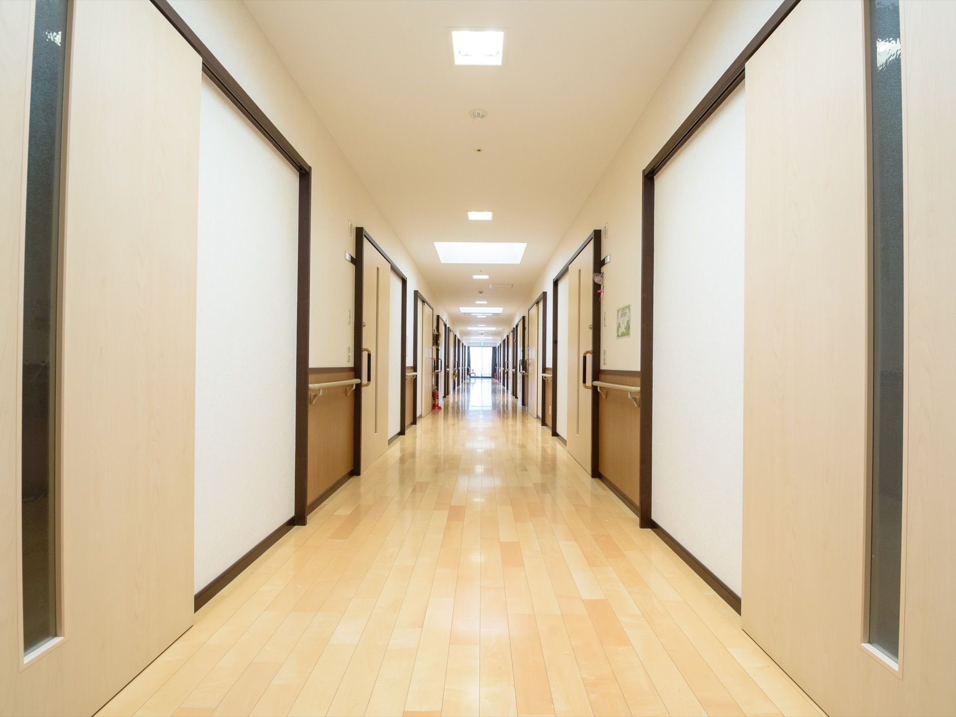 通路は照明、薄い色のフローリング、白色の壁で全体が明るくなっている。扉や手すりがあり、扉の一部は縦長の曇りガラスになっている。