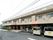 ２階建ての横に長い建物がある。建物の壁には施設名が書かれた大きな看板が掛かっている。前面部分は駐車スペースになっている。